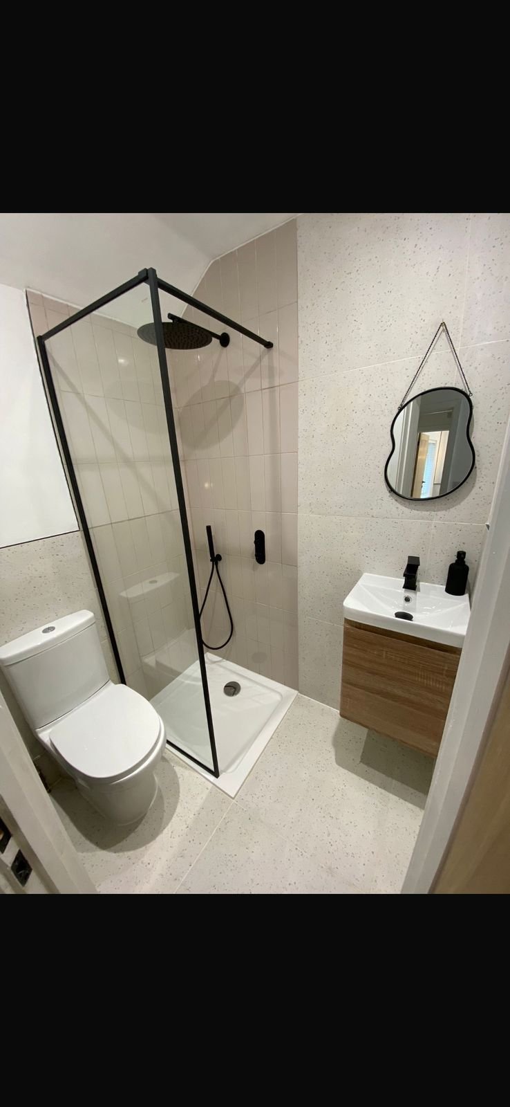 A shower room with a black framed screen and a wavy mirror