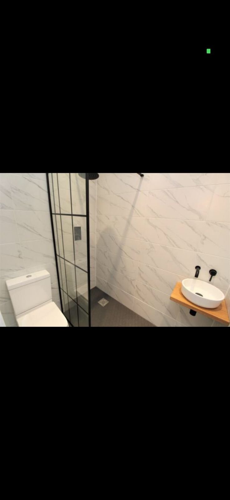 A shower room with a black framed screen and an oak shelf basin
