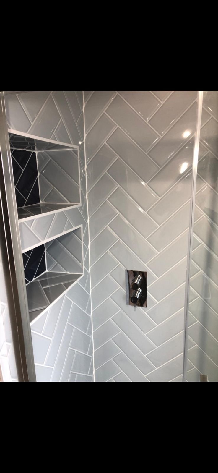 A shower with grey herringbone tiling and a tiled shelf