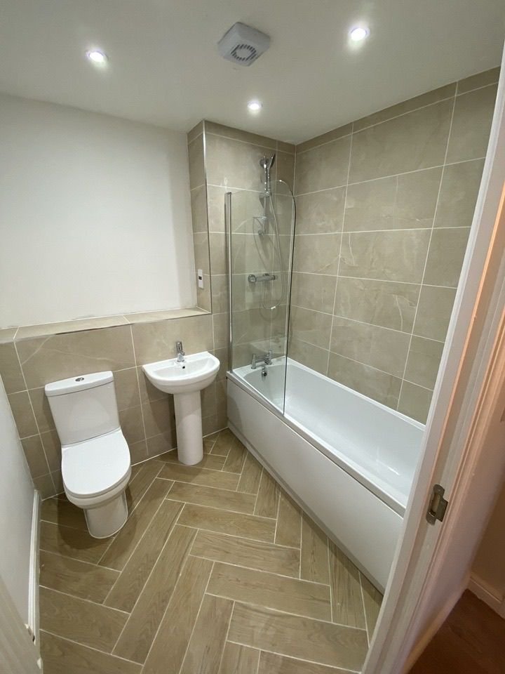 A bathroom with beige tiling and a shower over the bath