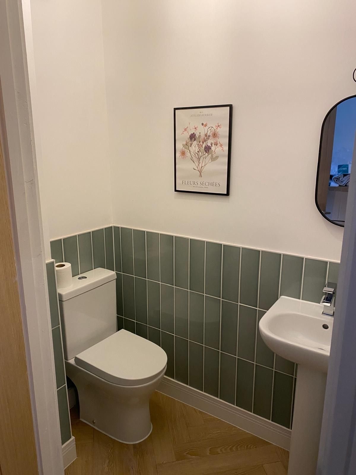 A cloakroom with green tiles and a pedestal basin